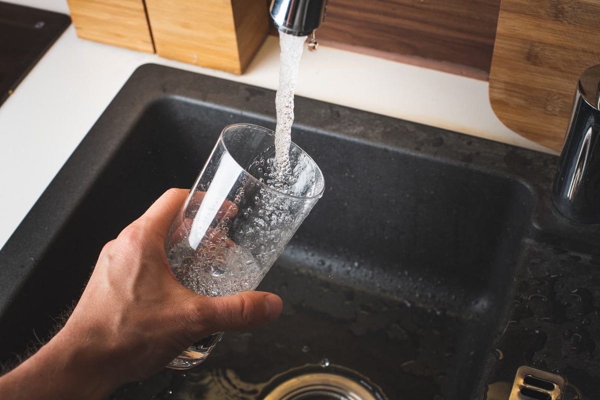 Glas wird in einer modernen Küche mit Wasser aus dem Küchenhahn gefüllt.