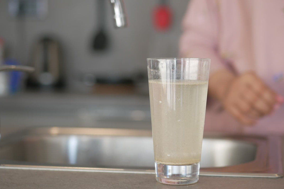 Leicht bräunlich verfärbtes Leitungswasser in einem Glas unter einem Küchenwasserhahn.