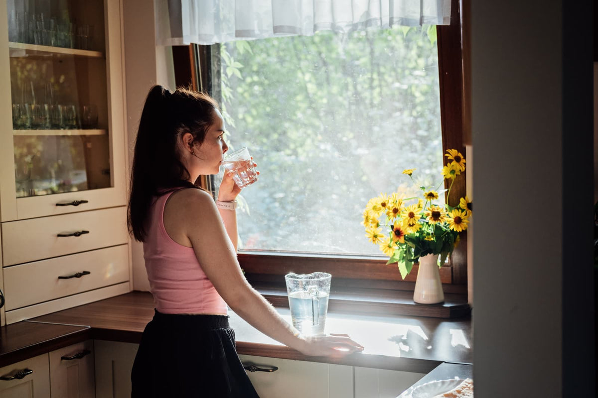 Person füllt in einer modernen Küche ein Glas Leitungswasser am Wasserhahn.