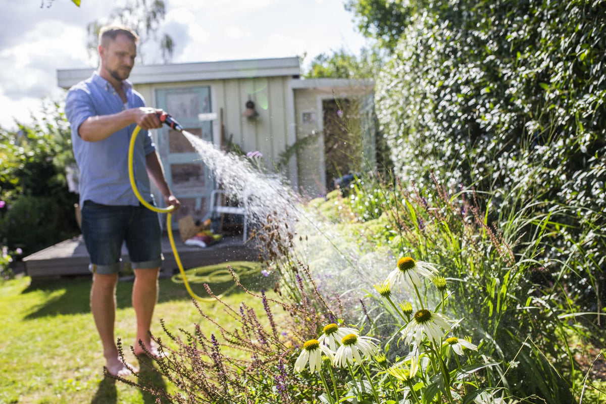 Mann gießt mit einem Gartenschlauch Blumen im Garten mit brunnenwasser, das möglicherweise einen hohen Eisengehalt aufweist.