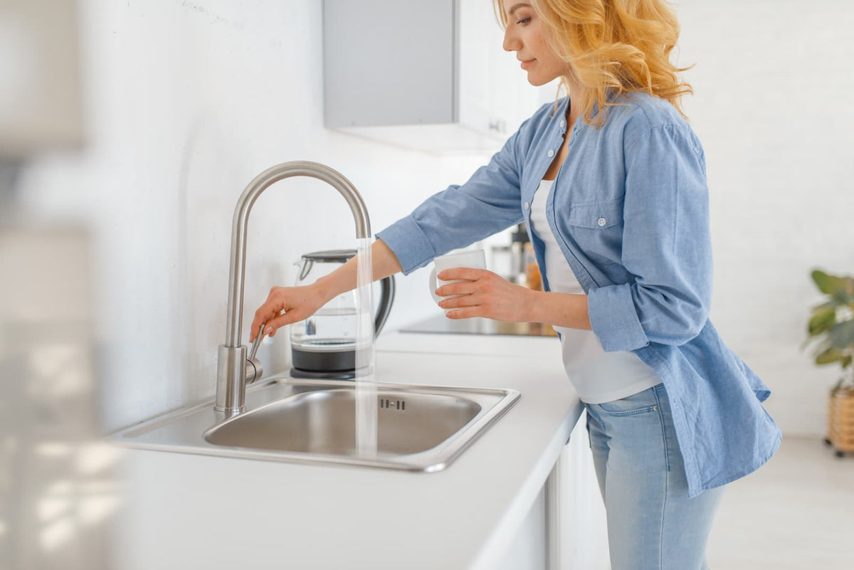 Frau füllt frisches Leitungswasser aus dem Küchenhahn in eine Tasse, mögliches eisenhaltiges Wasser aus der Hauswasserversorgung.