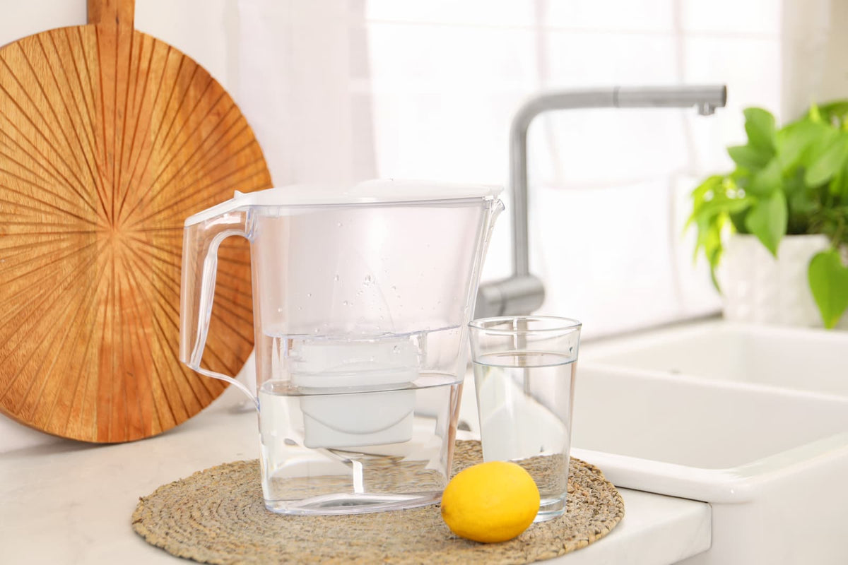 Transparente Wasserfilterkanne mit gefiltertem Wasser auf der hellen Küchenarbeitsplatte als Alternative zum Heiß‑Kalt‑Wasserspender für sauberes Trinkwasser.