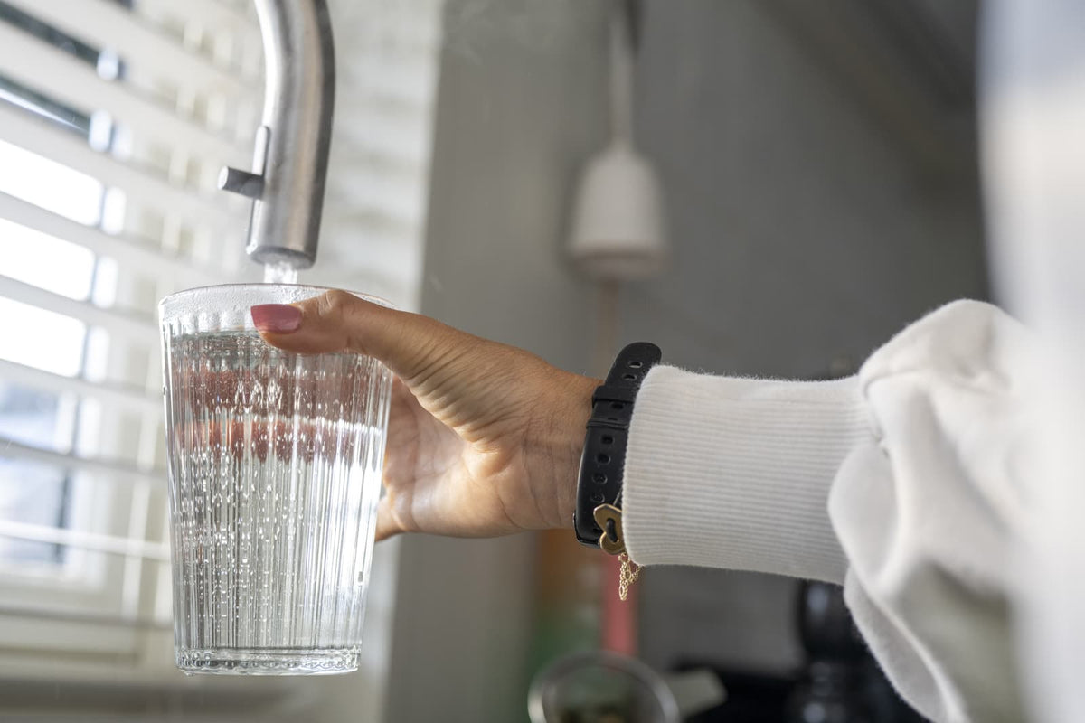 Person füllt in einer modernen Küche ein Glas Wasser am Wasserhahn.