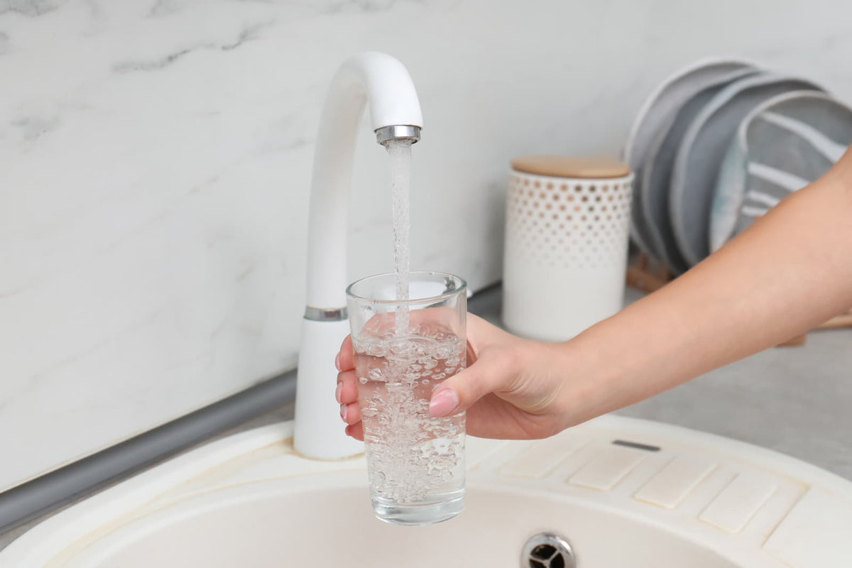 Ein Glas wird in einer modernen Küche mit Wasser aus dem Küchenhahn gefüllt.