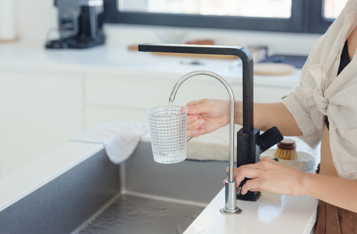 Glas Trinkwasser an einer modernen Küchenspüle mit Wasserhahn.