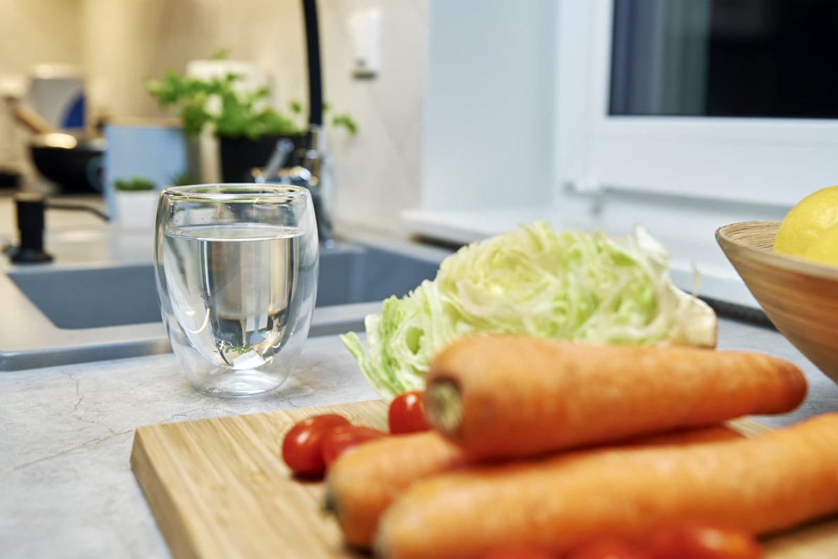 Glas mit Trinkwasser neben einem Küchenwasserhahn in einer modernen Küche.