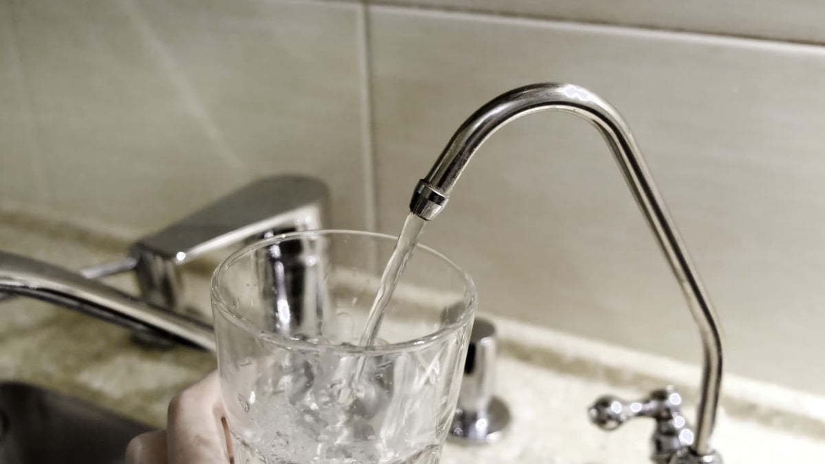 Ein Glas wird in einer modernen Küche mit Wasser aus dem Küchenhahn gefüllt.
