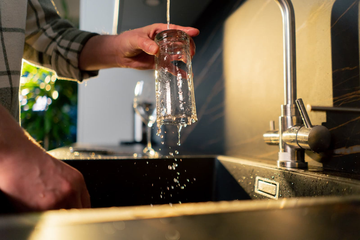 Person füllt in einer modernen Küche Trinkwasser in ein Glas.