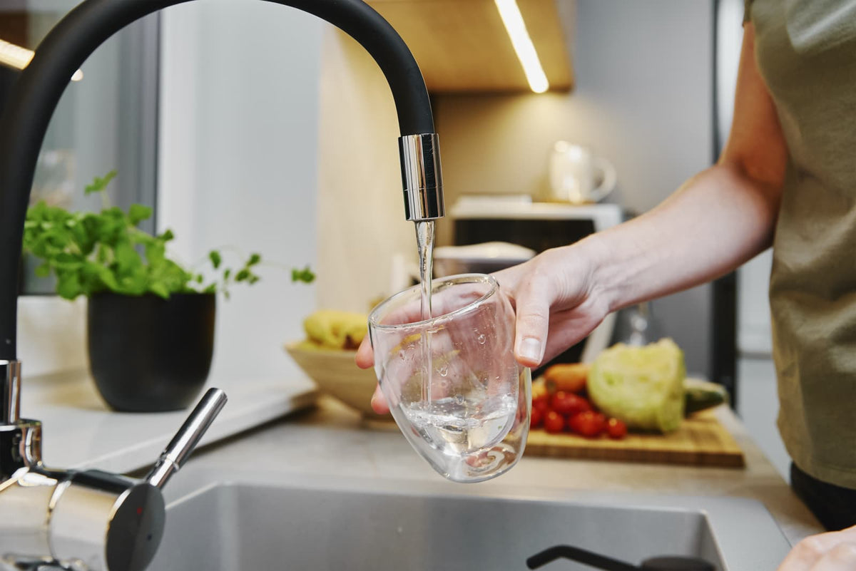 Eine Person füllt ein Glas mit frischem Wasser aus einer Küchenarmatur für aufbereitetes Trinkwasser im Haushalt.