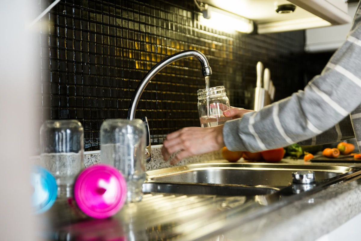 Glas mit Trinkwasser unter einem Küchenwasserhahn in einer modernen Wohnungsküche.
