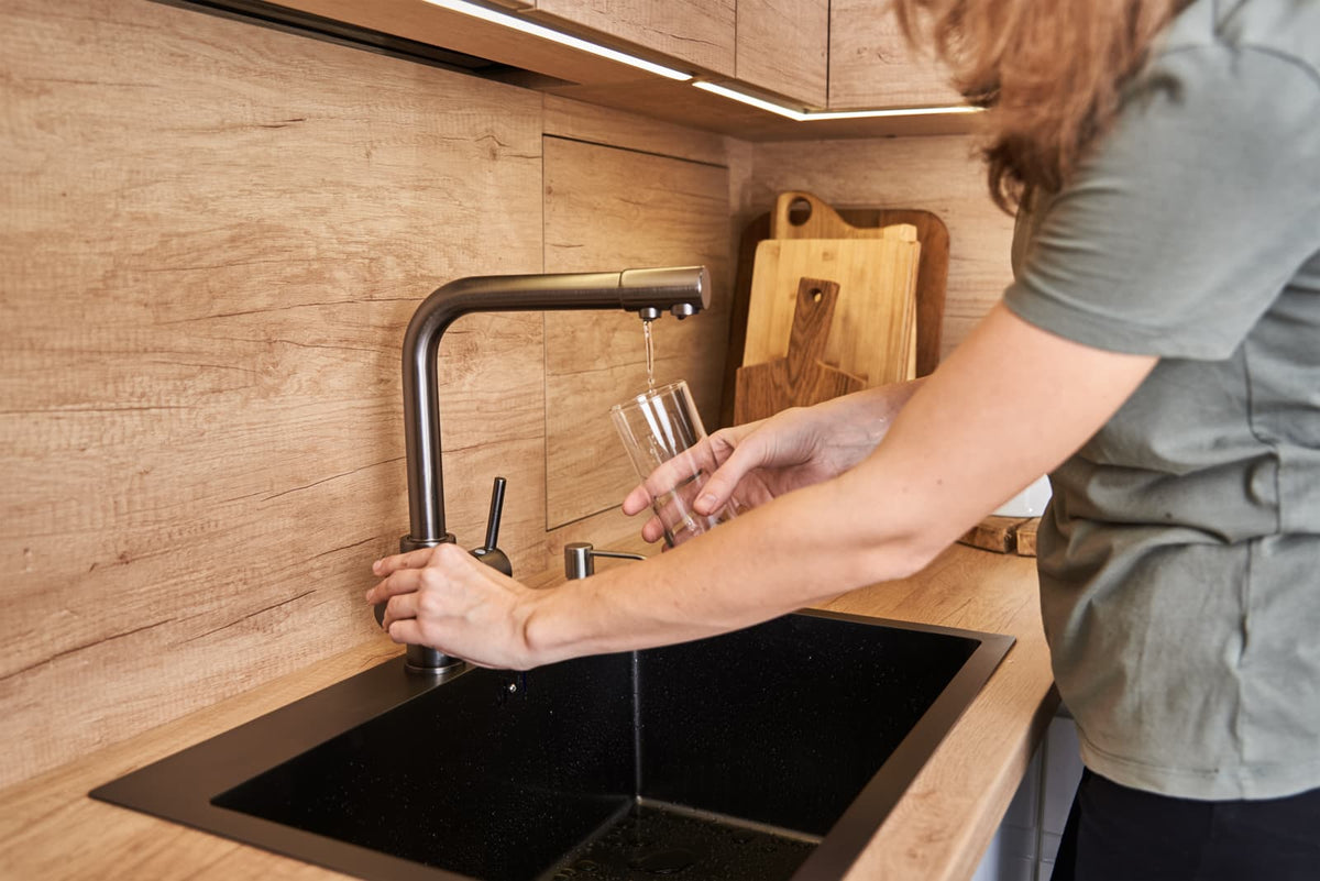Ein Glas Trinkwasser neben einem Küchenwasserhahn in einer modernen Wohnung.