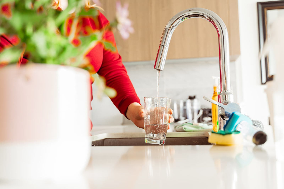 Frau füllt ein Glas mit frischem Wasser aus dem Küchenhahn, Darstellung für aufbereitetes Trinkwasser im Haushalt.
