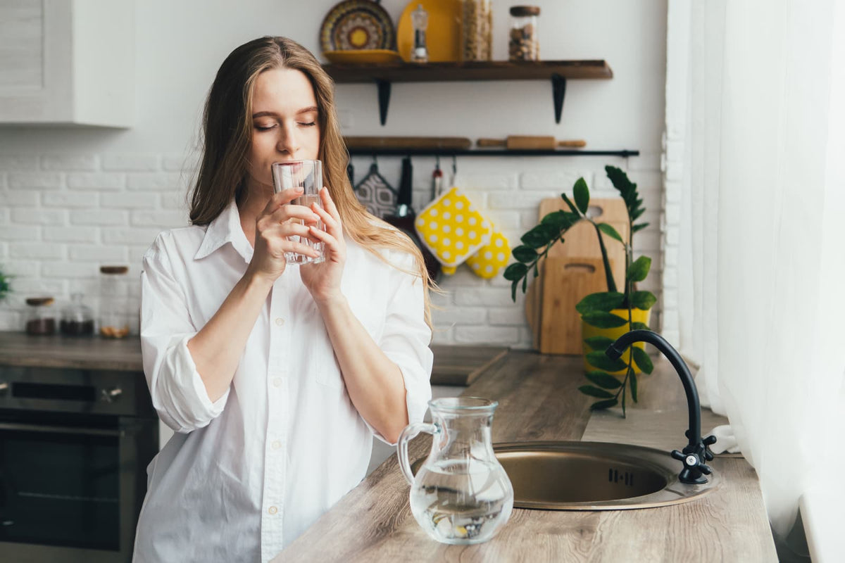 Person prüft ein Glas Leitungswasser neben einer Küchenspüle.