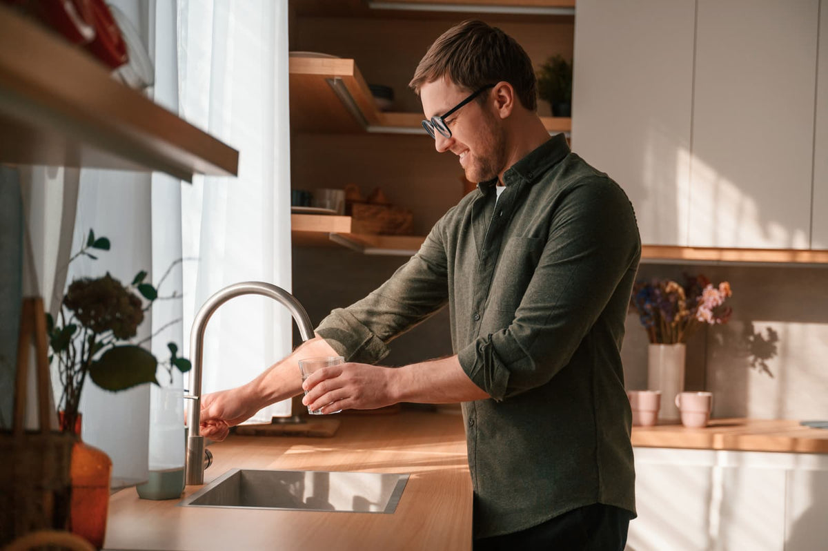 Ein Mann füllt in einer modernen Küche ein Glas mit gefiltertem Wasser, bevor der alte Wasserfilter fachgerecht entsorgt wird.