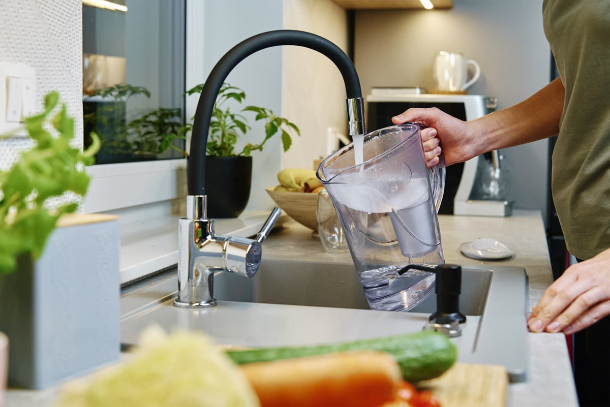 Person füllt einen Wasserfilterkanister mit gefiltertem Leitungswasser am Küchenhahn in einer modernen Küche.