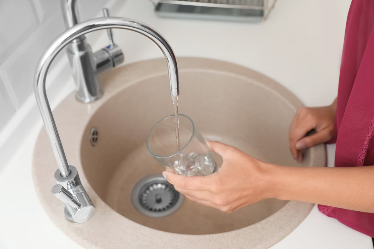 Eine Person füllt ein Glas mit frischem Leitungswasser aus einer modernen Küchenarmatur am Waschbecken, alltägliche Trinkwasserentnahme im Wohnbereich