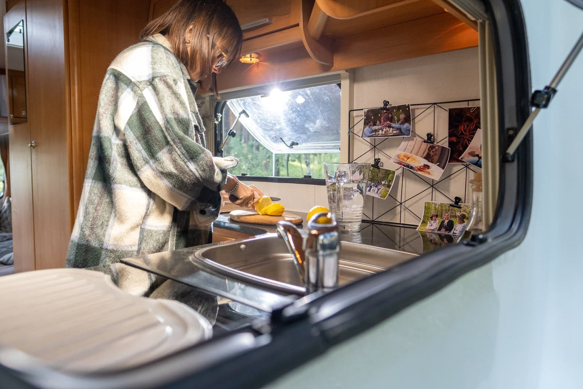 Eine Frau schneidet frische Zitrone in der Küche eines Wohnmobils, während sie mit dem Bord‑Trinkwasser kocht.